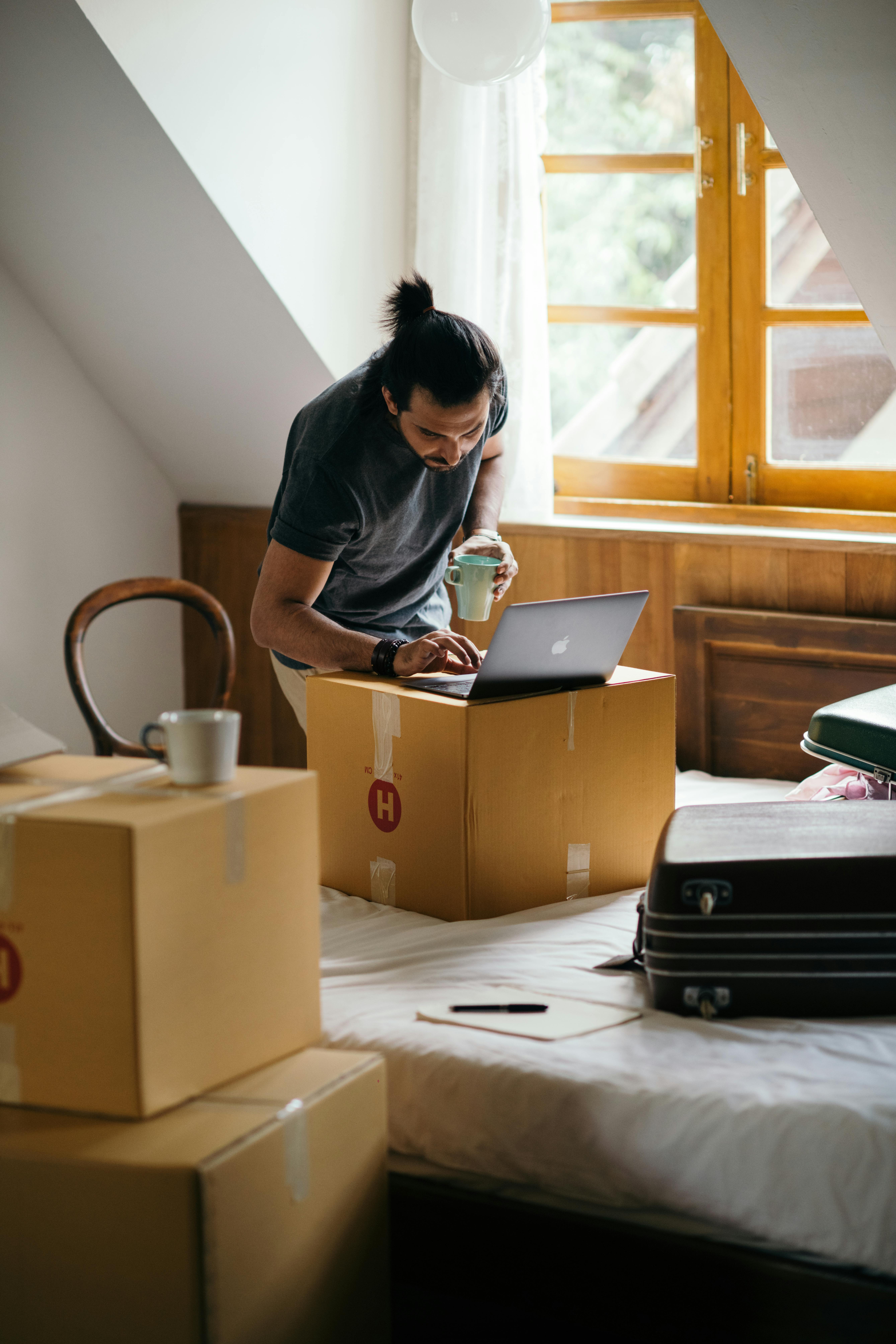 Man looking at a laptio with a coffee in hand surrounded by boxes.