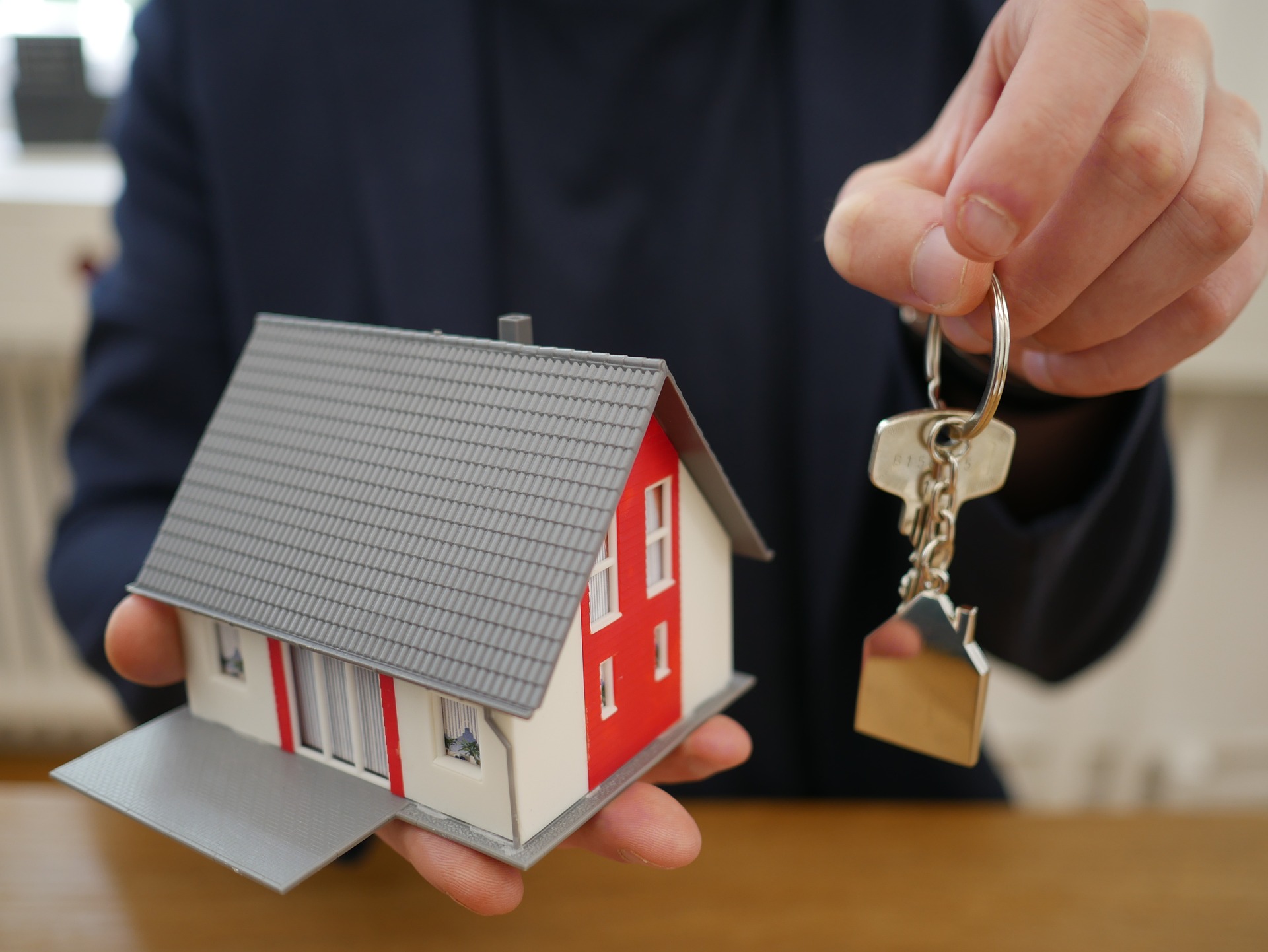 man holding small toy house and keys